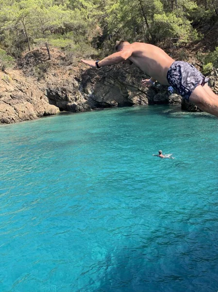 男は船の甲板から海に飛び込む 男は高さから水の中に飛び込む 岩によって地中海で泳いでいます トルコ フェティア12諸島ツアー 2021年7月12日 — ストック写真