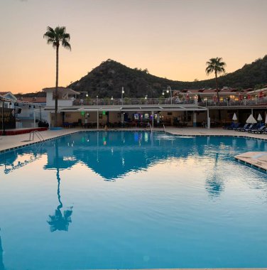 Dağların ve mavi gökyüzünün arka planında palmiye ağaçları. Bir yaz akşamında gün batımında uzun tropik ağaçlar. 