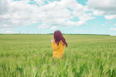 Parlak kızıl saçlı güzel kız buğday tarlasında mutlu. Küçük bulutsuz mavi gökyüzü, tarım ve köy kavramı