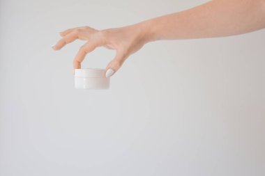 Beyaza izole edilmiş bir kadın elinde plastik krema kavanozu. Cilt gençliğini ve yaşlanma önleyici kremi yenilemek için profesyonel kozmetik ürünler. Deri bakımı konsepti. Kavanoz modeli