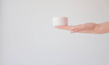 Beyaza izole edilmiş bir kadın elinde plastik krema kavanozu. Cilt gençliğini ve yaşlanma önleyici kremi yenilemek için profesyonel kozmetik ürünler. Deri bakımı konsepti. Kavanoz modeli.