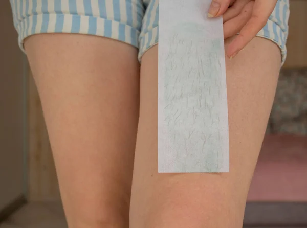 Leg waxing. Young woman waxing legs close up. Hair removal with wax at home.