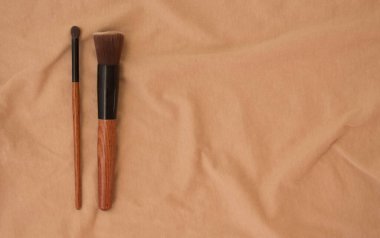 Makyaj fırçaları ve fırçalar bej kumaş dokusunun arka planında öğleden sonraları buruşmuş pamuk kıvrımlarıyla hayat bulur. Tasarımınız, web siteniz ve reklamlarınız için fotokopi alanı olan kozmetik set