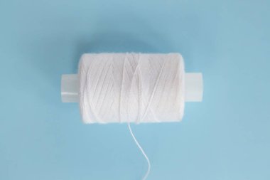 Üretim konsepti. Kıyafet tamiri, mevsim için yeni bir koleksiyon dikmek. Mavi arka planda beyaz iplik makarası. En küçük üst görünüm.