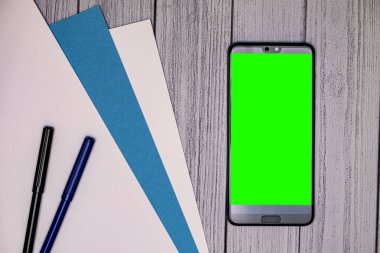 Kağıt ve keçeli kalemlerle cep telefonunun üst görüntüsü. Yeşil ekranlı cep telefonu modeli.