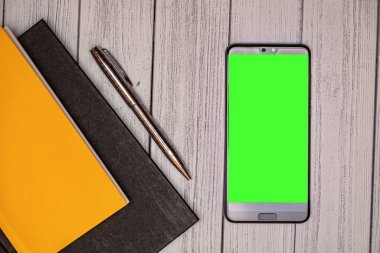Retro ahşap masada yakın plan yeşil ekran akıllı telefon. Not defteri, kalem ve cep telefonu iş yerinde. kopyalama alanı ile aynı hizada.