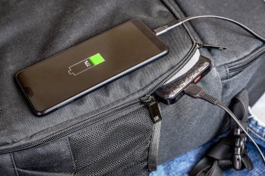 Güç bankasından akıllı telefonu şarj etmeye yakın çekim. Telefon sırt çantasının üzerinde, ve güç bankası da açık cepte..