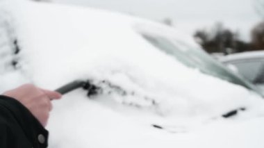 Bir adam arabanın ön camını kardan temizler. Arabanın içinde..