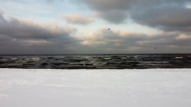 Kış denizi üzerinde güzel bir gün batımı ve karlı bir sahil. Karlı kışın deniz kenarında. Karlı kışın resimli doğası.