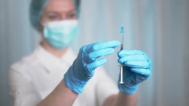 Doktor ilaç şırıngasından hava salıyor. Hemşire elinde Covid-19 ya da koronavirüs aşısı olan bir şırınga tutar. Şırıngayla eline odaklan..