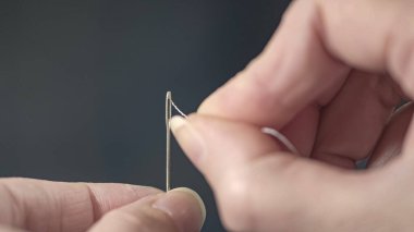 Bir terzinin ellerinin iğnenin gözüne iplik soktuğu yakın plan. Evde giysi tamiri.