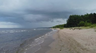 Deniz ve sahilin alçak açılı görüntüsü ve yağmur bulutları. Yuvarlanan dalgalarla kıyı şeridi perspektifi.