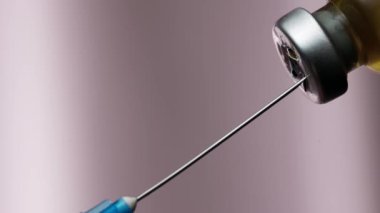 İğneli bir şırınga ilaç şişesinin kapağını deliyor. Şırınga aşıyı alıyor..