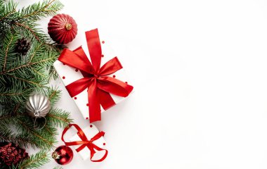 Beyaz arka planda Noel kompozisyonu. Beyaz hediye kutuları, içinde köknar dalları ve oyuncaklar olan kırmızı kurdele var. Tebrik etmek için fotokopi alanının üstünü göster