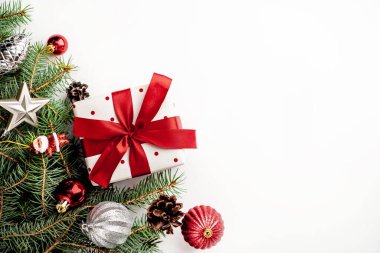 Beyaz arka planda Noel kompozisyonu. Beyaz hediye kutusu, içinde köknar dalları ve oyuncaklar olan kırmızı kurdele var. Tebrik etmek için fotokopi alanının üstünü göster