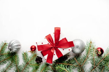 Beyaz arka planda Noel kompozisyonu. Beyaz hediye kutusu, içinde köknar dalları ve oyuncaklar olan kırmızı kurdele var. Tebrik etmek için fotokopi alanının üstünü göster