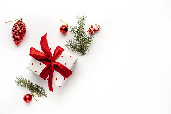 白いギフトボックス付きの白い背景のクリスマスの組成 モミの枝 おもちゃ あなたのお祝いのためのコピースペースを持つ赤いリボン — ストック写真