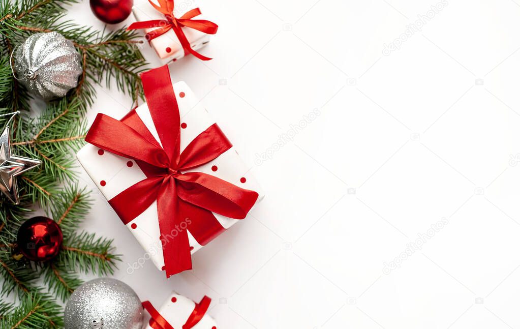 Christmas composition on a white background with a white gift boxes with a red ribbon with fir branches, toys. View top with copy space for your congratulations