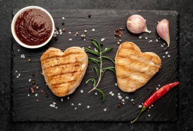 Kalpler şeklinde ızgara tavuk bifteği ve arka planda baharatlar ve otlar. 