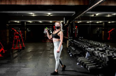 Spor salonunda spor yaptıktan sonra maske takan genç bir kadın.