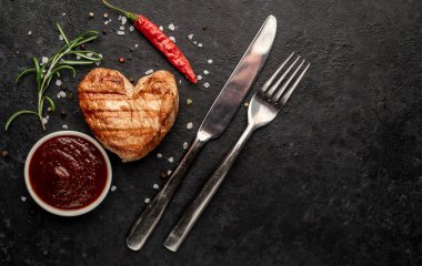 Kalp şeklinde ızgara tavuk bifteği, arka planda baharatlar ve otlar. 