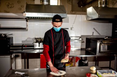 Şef koruyucu maske takıyor, pizza için hamur yapıyor, yemek pişiriyor. 