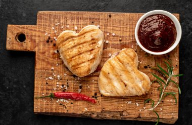 Kalpler şeklinde ızgara tavuk bifteği ve arka planda baharatlar ve otlar. 