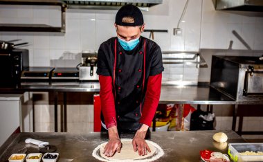 Şef koruyucu maske takıyor, pizza için hamur yapıyor, yemek pişiriyor. 