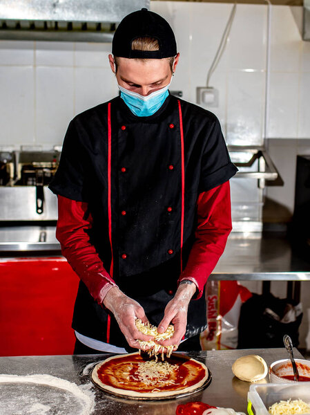 View of chef wearing protective mask making pizza at kitchen, cooking concept