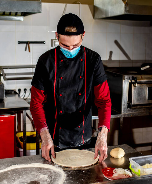 View of chef wearing protective mask making dough for pizza at kitchen, cooking concept
