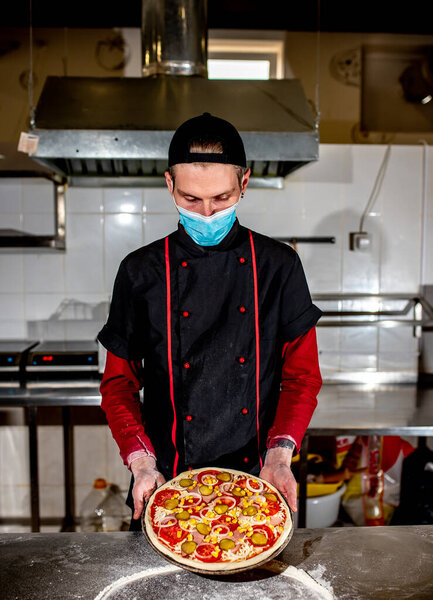 View of chef wearing protective mask making pizza at kitchen, cooking concept
