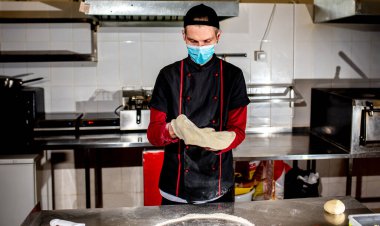 Şef koruyucu maske takıyor, mutfakta pizza yapıyor, yemek pişiriyor. 