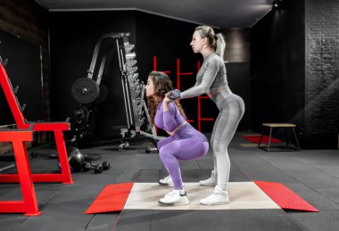 Spor salonunda halterle egzersiz yapan iki genç kadın.