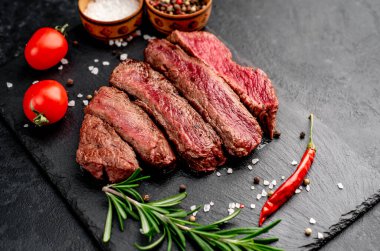 Siyah arka planda baharatlı dilimlenmiş biftek. 