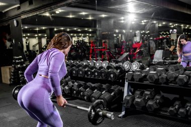 Spor salonunda halterle egzersiz yapan genç bir kadın.