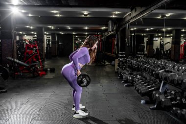 Spor salonunda halterle egzersiz yapan genç bir kadın.