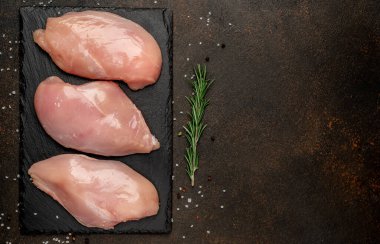 Siyah tahta yüzeyinde biberiyeli çiğ tavuk filetosu.