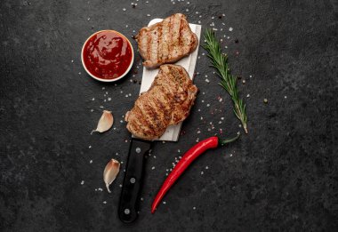 Bıçakta ızgara et, baharat ve siyah taş masada otlar.