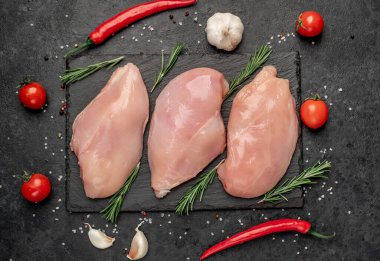 Çiğ tavuk göğsü, otlar ve baharatlar siyah tahtada.