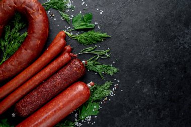 Otlu çiğ sosisler ve siyah arkaplanda tuz.