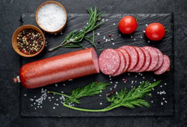 Otlu salam, siyah arkaplanda tuz ve baharat.