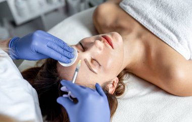 Kozmetik uzmanı kalıcı yüz tedavisi yapıyor. Genç güzellik uzmanının yüzünde lazer darbesi alan kadın..