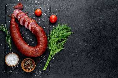 Siyah yüzeyde domatesli çiğ sosis, biberiye ve baharatlar.