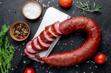 Siyah yüzeyde domatesli salam, biberiye ve baharatlar.