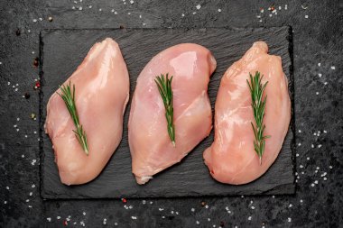 Siyah tahta yüzeyinde biberiyeli çiğ tavuk filetosu.
