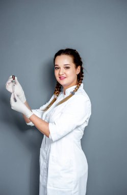 Gri arka planda steteskobu olan genç bir kadın doktor.