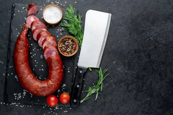 Otlu salam, tuz ve baharat ile siyah arkaplan üzerinde bıçak ile