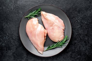 Biberiyeli çiğ tavuk göğsü ve siyah arka planda baharatlar.