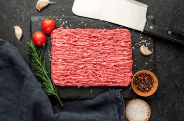 Baharatlı çiğ et ve siyah arka planda otlar.