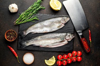 Baharatlı çiğ dorado balığı ve siyah arka planda otlar.